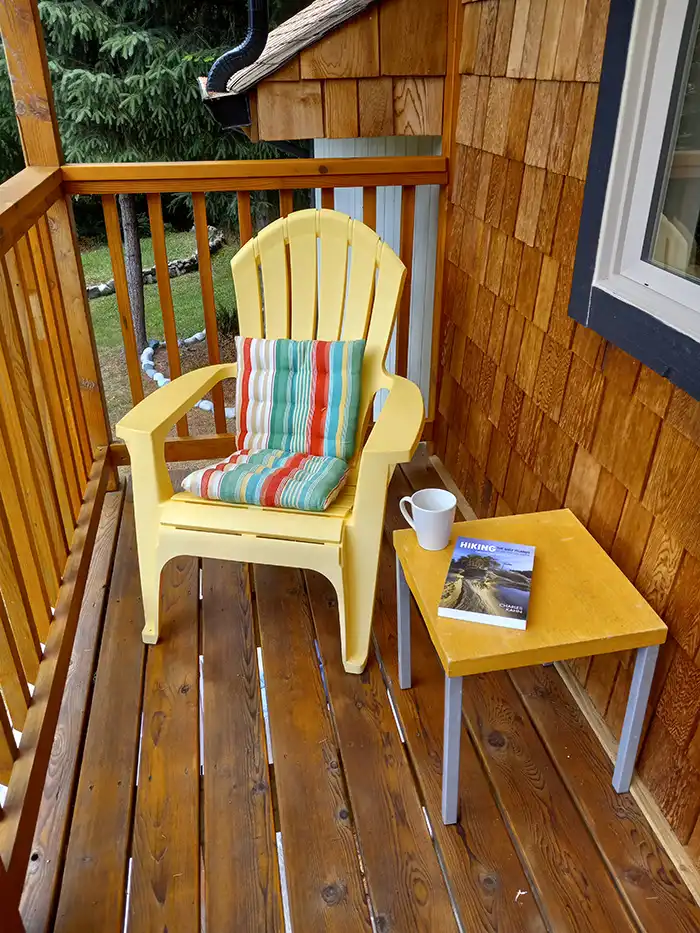 A photo of an Adirondack chair on the balcony, with a cup of coffee and a book on the side table