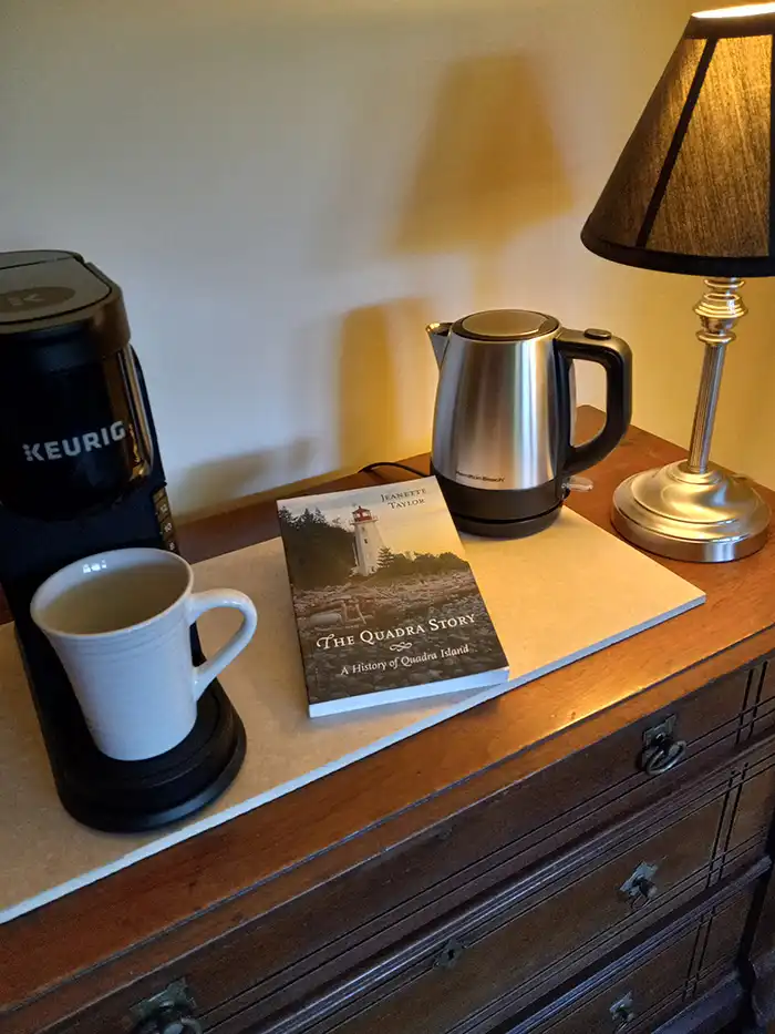 A photo of a Keurig machine and an electric kettle on top of a dresser with a book on the history of Quadra Island